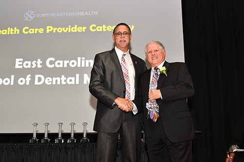 Craig Slotke, DDS, faculty director of the ECU School of Dental Medicine’s Community Service Learning Center-Robeson County (at right), accepted an award on behalf of his dental team from Joseph Roberts Jr., MD, vice president of Southeastern Health, during Southeastern Health’s 2018 Regional Community Health Awards night on October 23 in Lumberton, N.C.