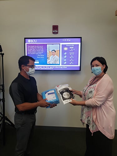 Nicole Alley, right, SoDM clinic administrator, hands masks and gowns to Dr. Norberto Velazquez, adjunct faculty member and practitioner at Drs. Davila & Velazquez, P.A. in Greenville. 