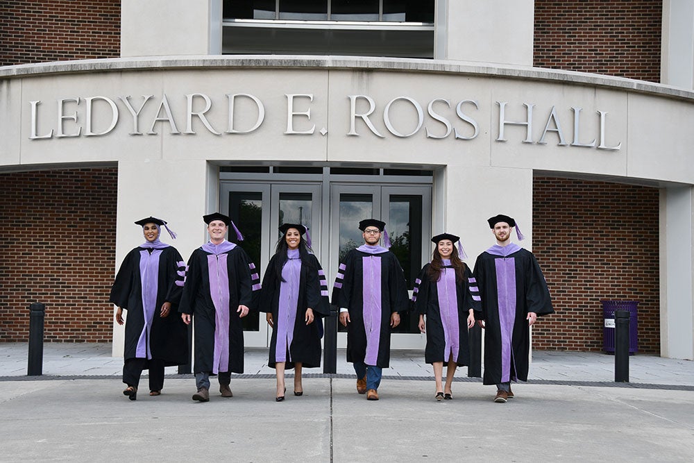 Students wearing graduation attire in front of Ross Hall front entrance.