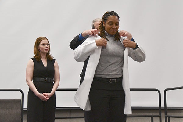 Man helping a woman put on her white coat. 