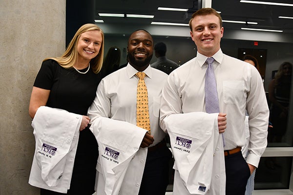 Three people posing for photo holding white coats.