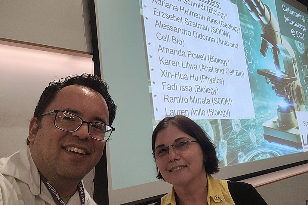 Two professors posing in front of a digital display screen.