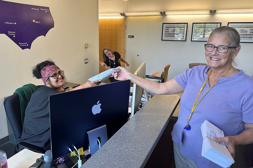 Woman handing an envelope to a woman at a desk.