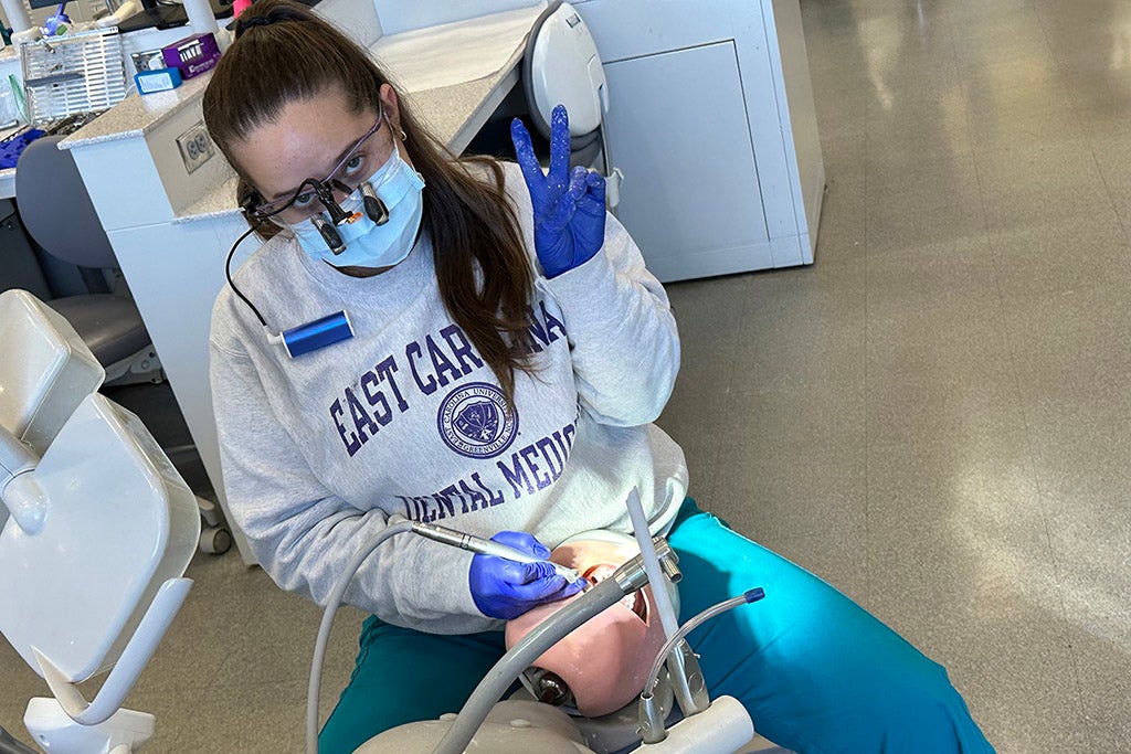 Student working on a mannequin giving the peace sign.