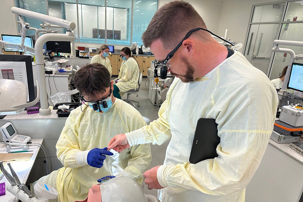 Two men working on a dental mannequin head.