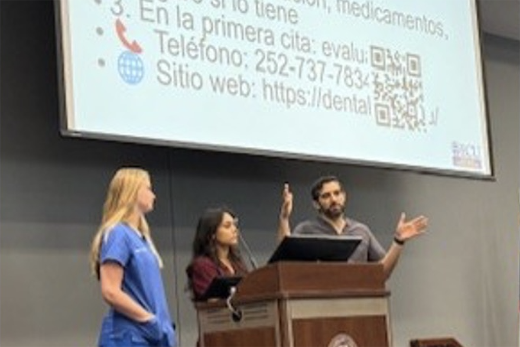 People presenting in front of a large tv screens with Spanish words.