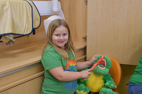 A photo of a young girl holding a toothbrush and a stuffed toy animal in a dental clinic.