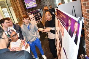 A photo of a student describing her poster presentation to a group of students.