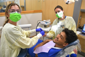 Students dentists working on a patient in a chair.