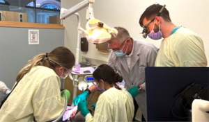 Dentist and students gathered around a patient. 