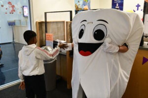 Person dressed as a tooth give a kid a high five